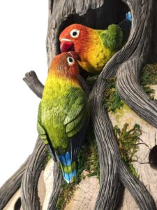 Escultura pareja de loritos en árbol picoteándose